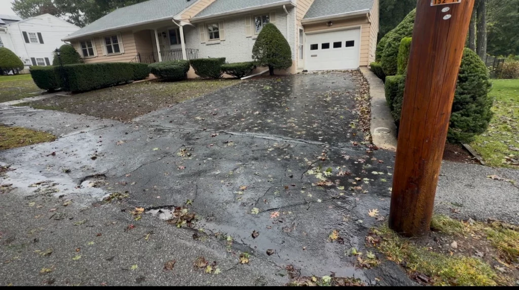 rain-soaked asphalt driveway in Stoneham, MA before paving, leading to a single-car garage.