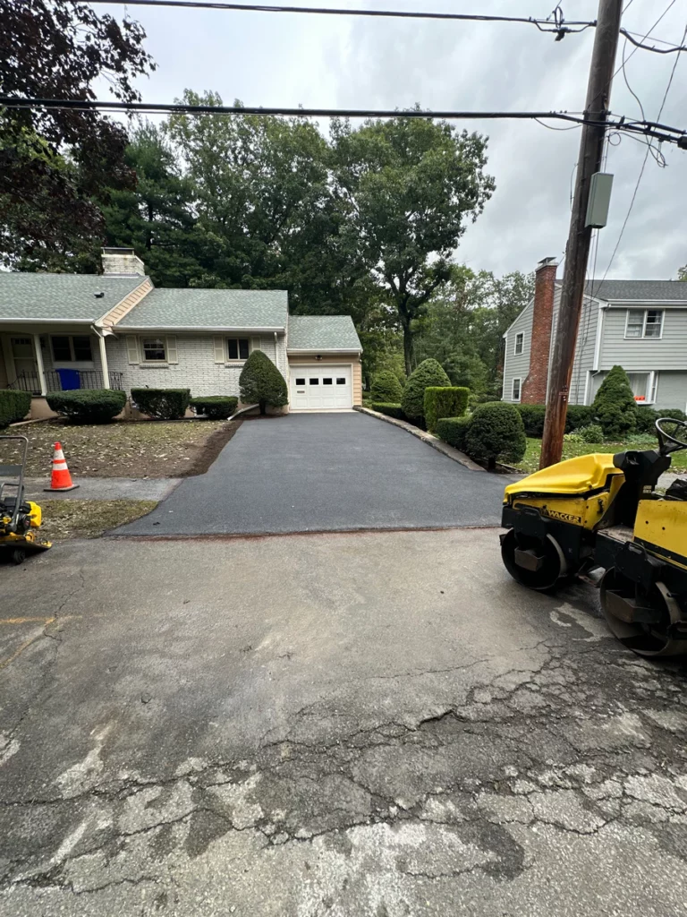 Freshly paved asphalt driveway in Stoneham, MA with a double drum roller and plate compactor at the street.