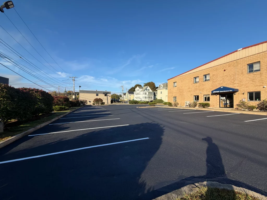 Sealcoated commercial parking lot in Woburn, MA with fresh white stall lines beside a two-story block building.