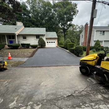 Freshly paved asphalt driveway in Stoneham, MA with a double drum roller and plate compactor at the street.