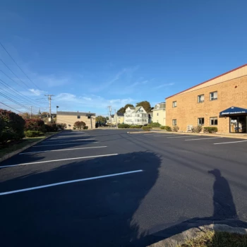 Sealcoated commercial parking lot in Woburn, MA with fresh white stall lines beside a two-story block building.